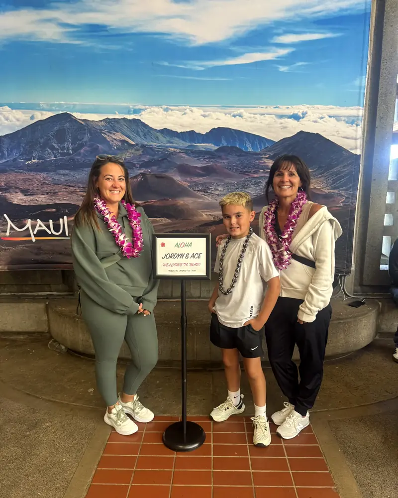Three travelers wearing orchid lei beside their welcome sign