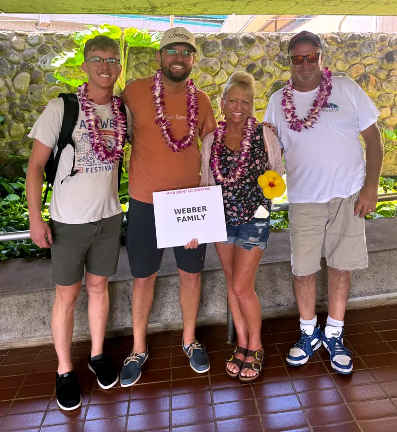 Family of four wearing orchid lei, holding their welcome sign
