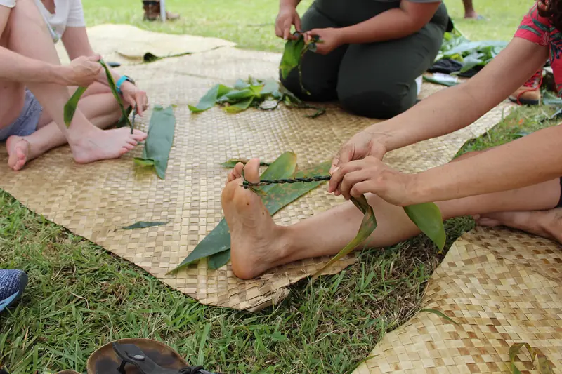 A festival-goer twisting a lei from fresh ti leaves
